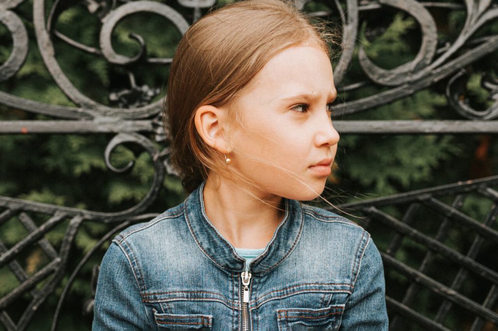 thoughtful scowl candid eight year old kid girl sits on bench and observe nature. prepubertal age of children and lives, mind psychology and mental health. fashion clothes. geometric shapes. banner